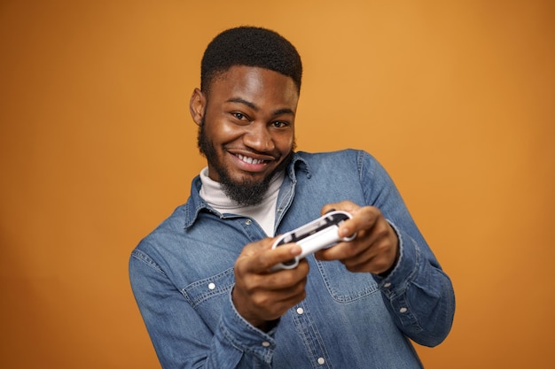 Young african american man holding joystick playing video games yellow background