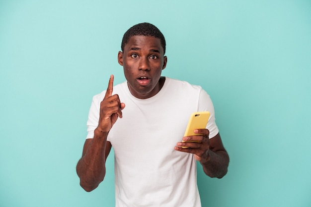 Young African American man holding a mobile phone isolated on blue background having an idea, inspiration concept.