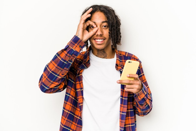 Young African American man holding mobile phone isolated on white background excited keeping ok gesture on eye