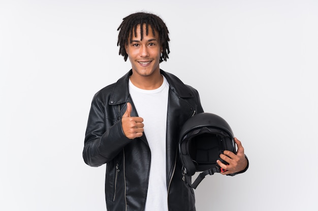 Young african american man holding a motorcycle helmet isolated on white wall with thumbs up because something good has happened