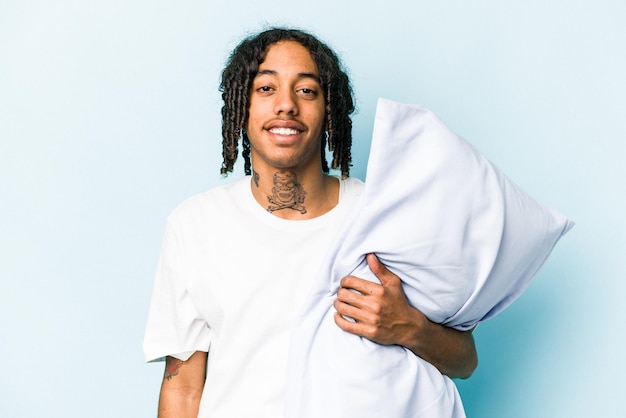 Young African American man holding a pillow isolated on blue background happy smiling and cheerful