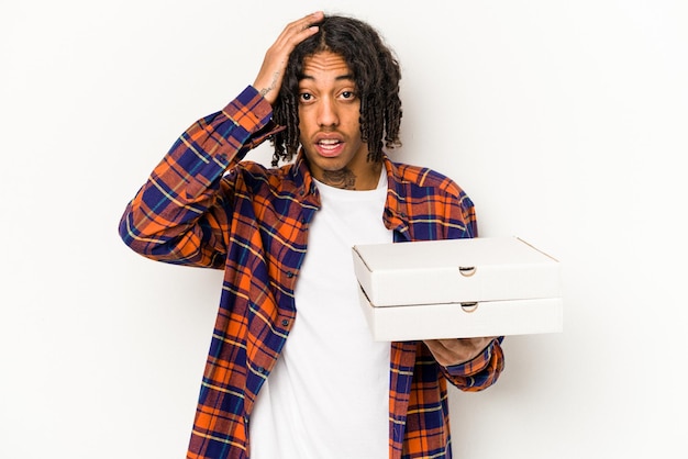 Young African American man holding pizzas isolated on blue background being shocked she has remembered important meeting