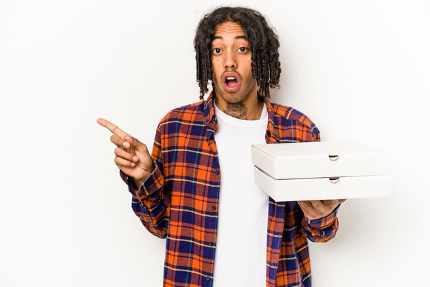 Молодой афроамериканец держит пиццу на синем фоне, указывая в сторону