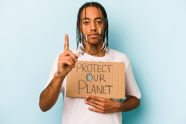 Young African American man holding protect our planet placard isolated on blue background