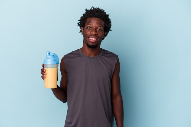 Young african american man holding protein milkshake isolated on blue background happy, smiling and cheerful.