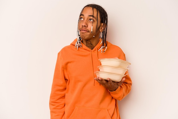 Young African American man holding tupperware isolated on white background dreaming of achieving goals and purposes