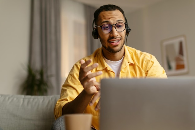 사진 웹캠에 앉아 소파에 앉아 노트북을 사용하여 웹 통화를 하는 헤드셋을 쓴 젊은 아프리카계 미국인 남자