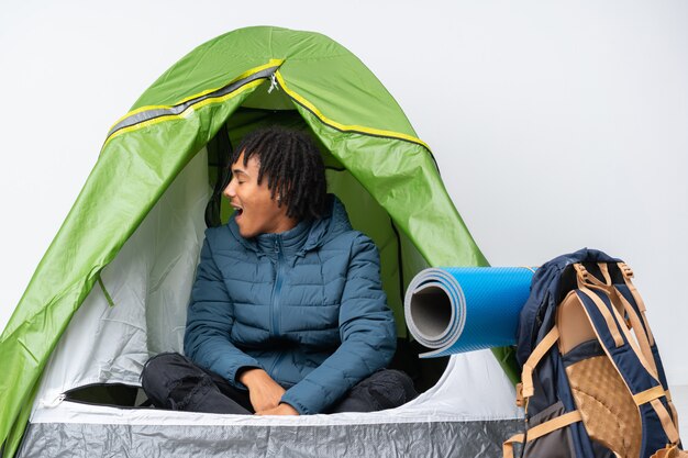 young african american man inside a camping green tent laughing in lateral position