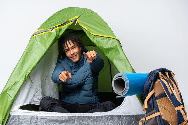 young african american man inside a camping green tent points finger at you while smiling