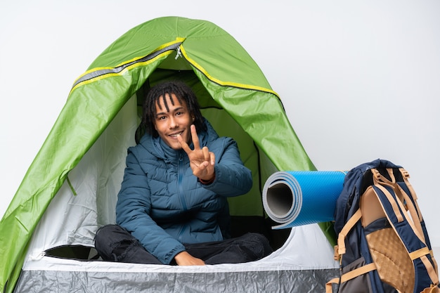 young african american man inside a camping green tent smiling and showing victory sign