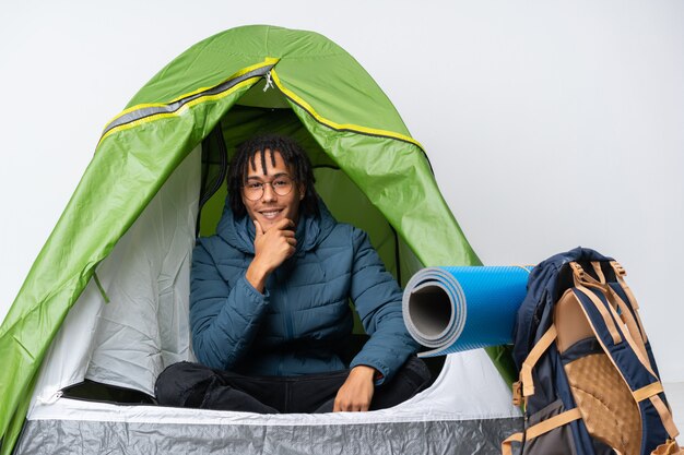 Foto giovane uomo afroamericano dentro una tenda verde di campeggio con i vetri e sorridere