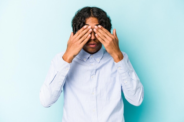 Young African American man isolated on blue background afraid covering eyes with hands