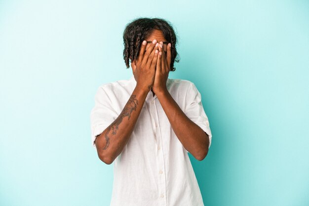 Photo young african american man isolated on blue background blink at the camera through fingers, embarrassed covering face.