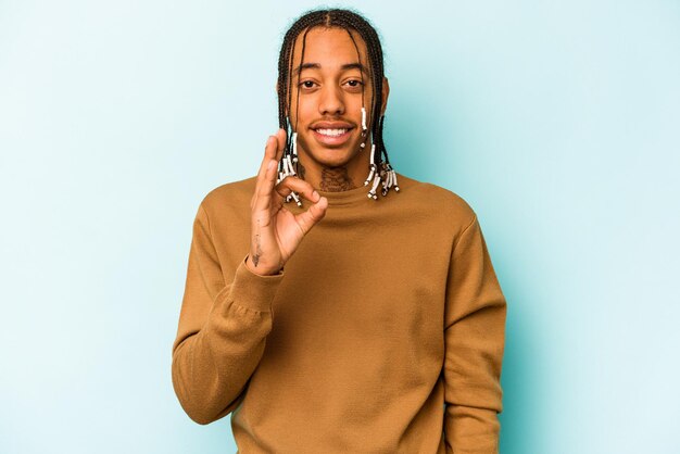 Young African American man isolated on blue background cheerful and confident showing ok gesture