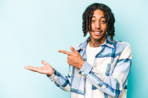 Young African American man isolated on blue background excited holding a copy space on palm