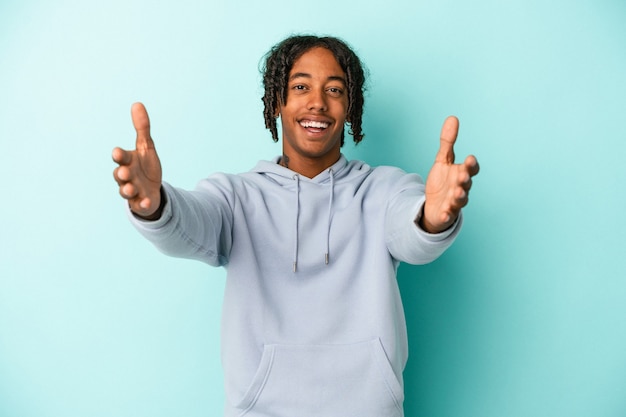 Young african american man isolated on blue background feels confident giving a hug to the camera.