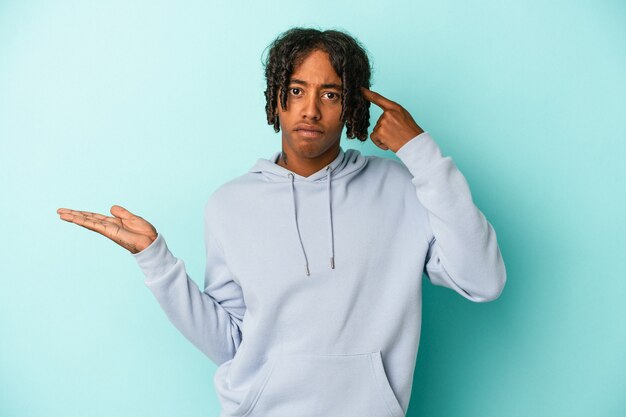 Young african american man isolated on blue background holding and showing a product on hand.