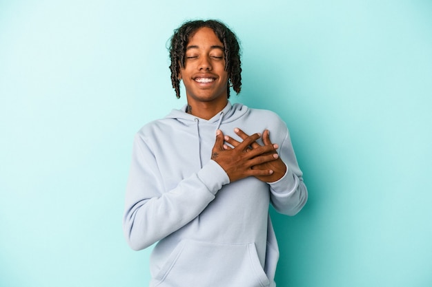 Young african american man isolated on blue background laughing keeping hands on heart, concept of happiness.
