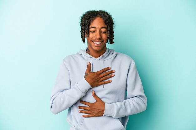 Young african american man isolated on blue background laughs happily and has fun keeping hands on stomach.