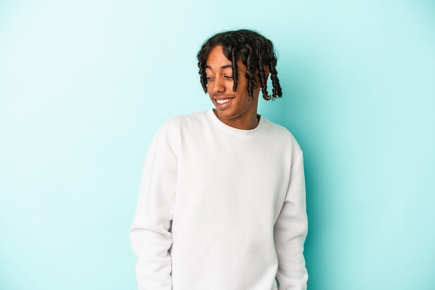 Young african american man isolated on blue background looks aside smiling, cheerful and pleasant.