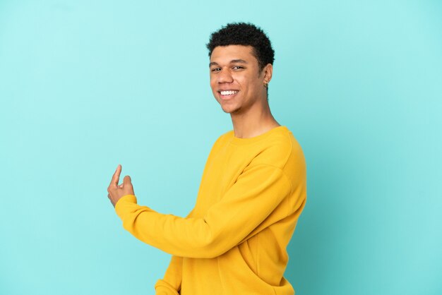 Молодой афро-американский мужчина, изолированные на синем фоне, указывая назад