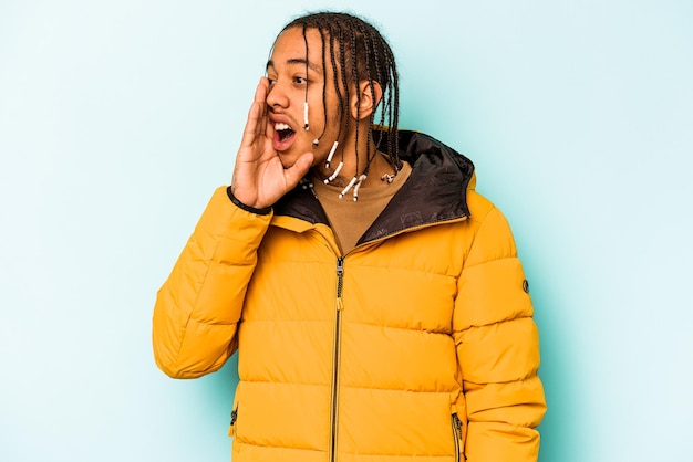 Young African American man isolated on blue background shouting and holding palm near opened mouth