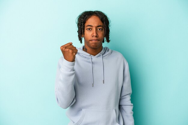 Young african american man isolated on blue background showing fist to camera, aggressive facial expression.