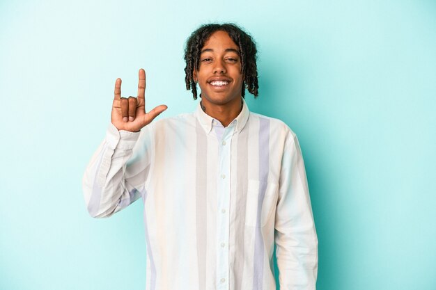 Young african american man isolated on blue background showing a horns gesture as a revolution concept.