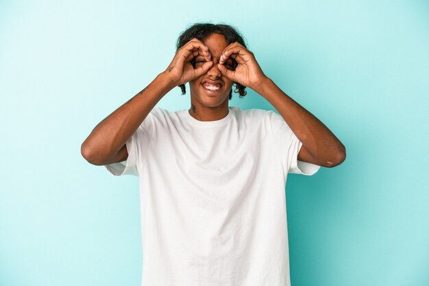 Young african american man isolated on blue background showing okay sign over eyes