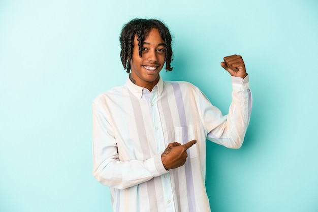 Young african american man isolated on blue background showing strength gesture with arms, symbol of feminine power