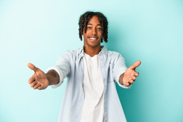 Young african american man isolated on blue background showing a welcome expression.