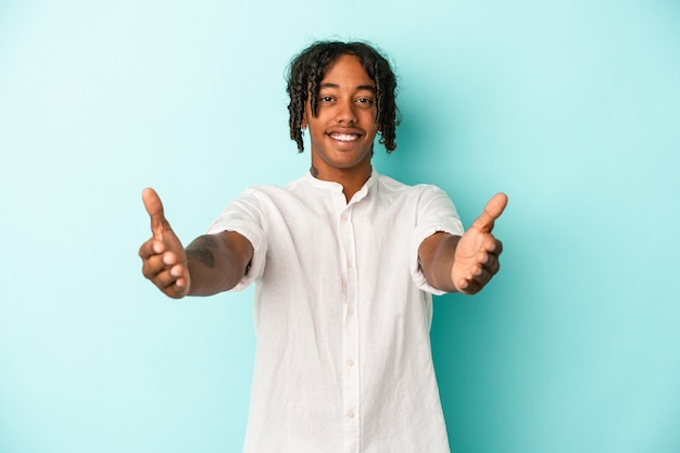 Young african american man isolated on blue background showing a welcome expression.