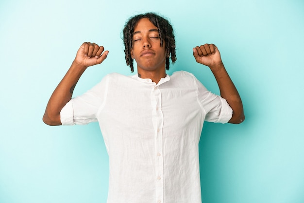 Young african american man isolated on blue background stretching arms, relaxed position.