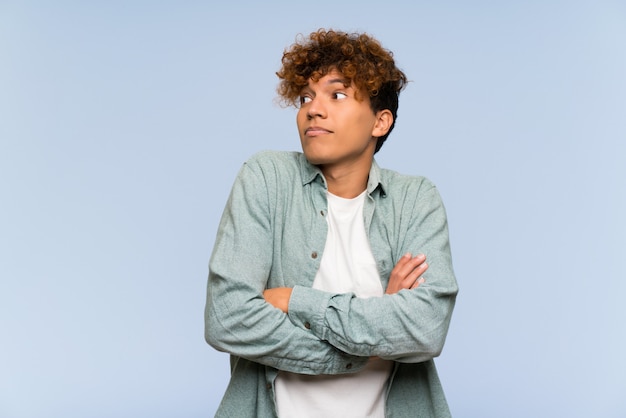 Young african american man over isolated blue wall making doubts gesture while lifting the shoulders