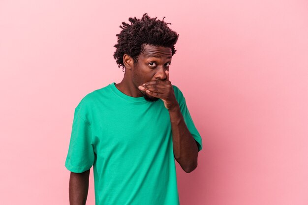 Young african american man isolated on pink background covering mouth with hands looking worried.