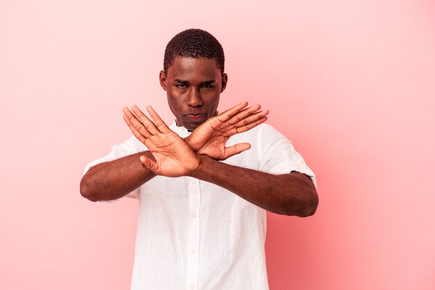 Giovane uomo afroamericano isolato su sfondo rosa che fa un gesto di rifiuto