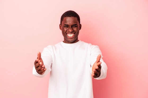Young African American man isolated on pink background feels confident giving a hug to the camera.