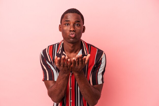 Young African American man isolated on pink background folding lips and holding palms to send air kiss.