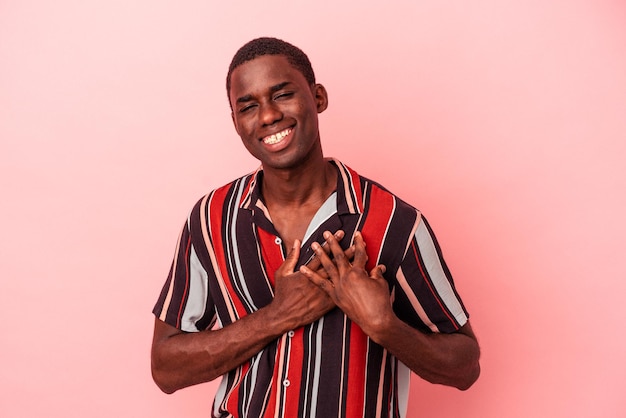 Young African American man isolated on pink background has friendly expression, pressing palm to chest. Love concept.