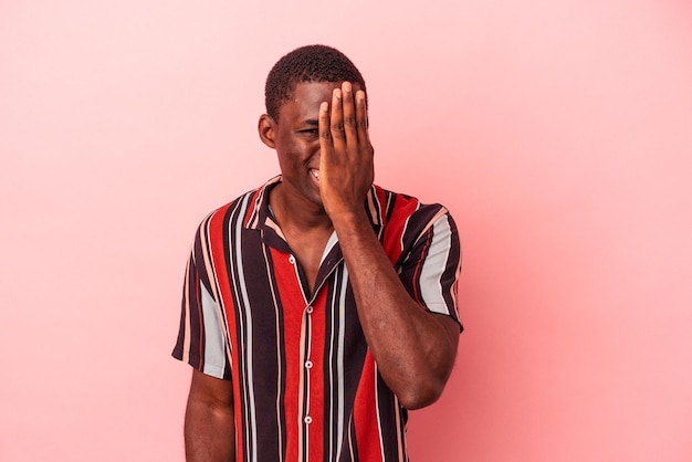 Young African American man isolated on pink background having fun covering half of face with palm