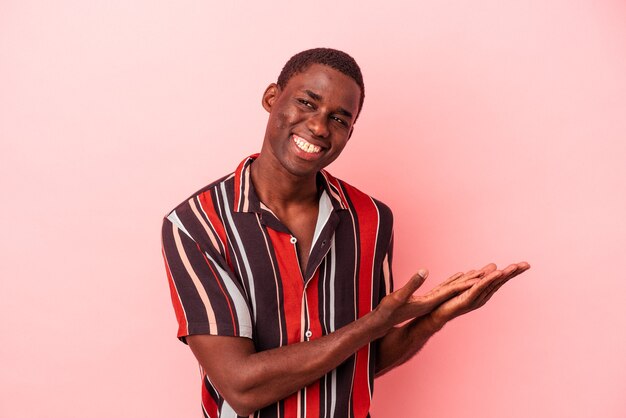 Young African American man isolated on pink background holding a copy space on a palm.