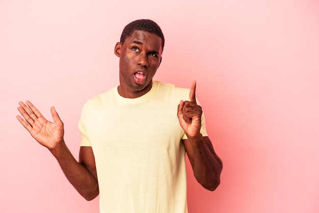 Young African American man isolated on pink background holding and showing a product on hand.