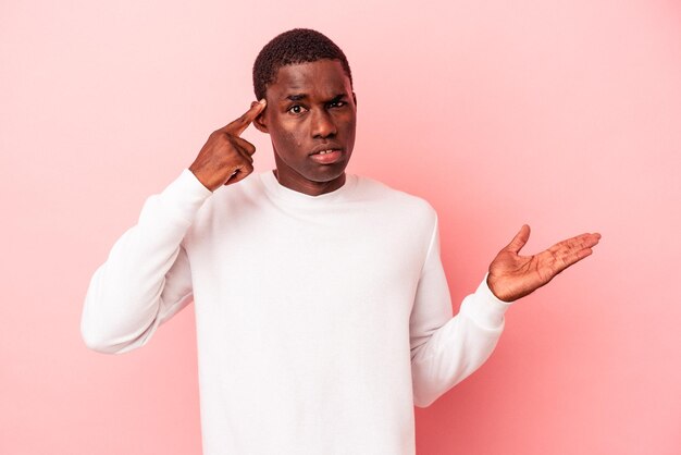 Young African American man isolated on pink background holding and showing a product on hand