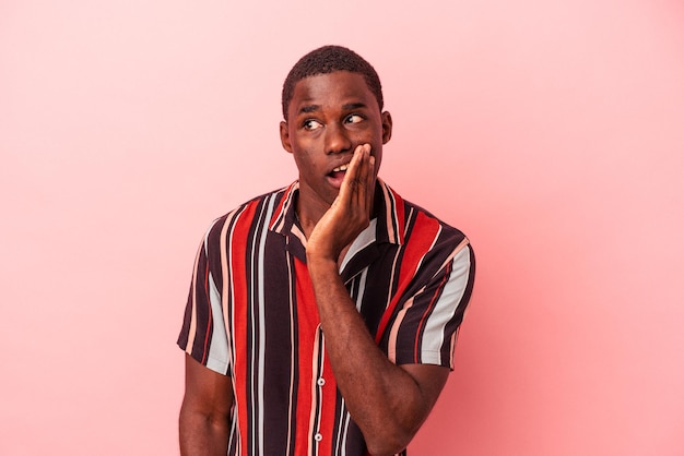 Young African American man isolated on pink background is saying a secret hot braking news and looking aside