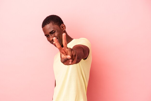 Young African American man isolated on pink background joyful and carefree showing a peace symbol with fingers.