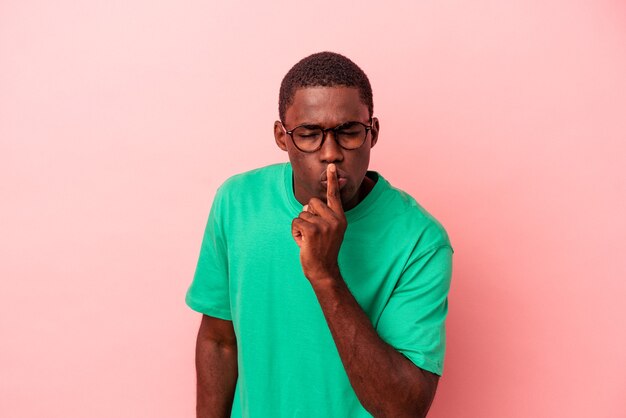 Young African American man isolated on pink background keeping a secret or asking for silence.