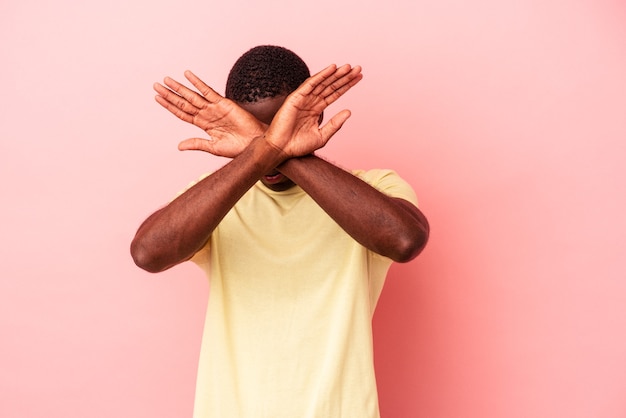 Young African American man isolated on pink background keeping two arms crossed, denial concept.