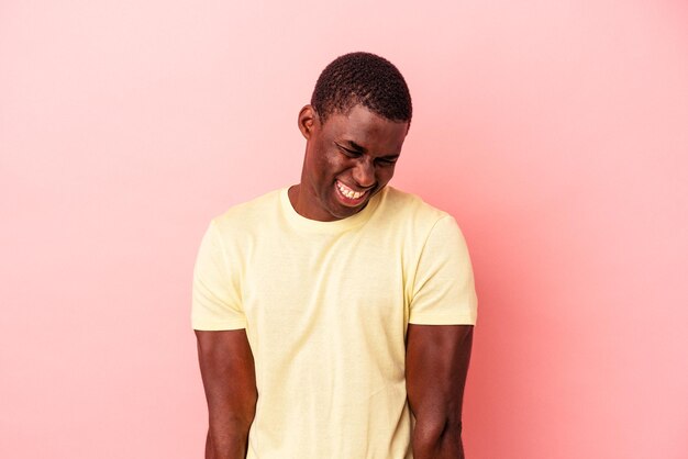 Young African American man isolated on pink background laughs and closes eyes, feels relaxed and happy.