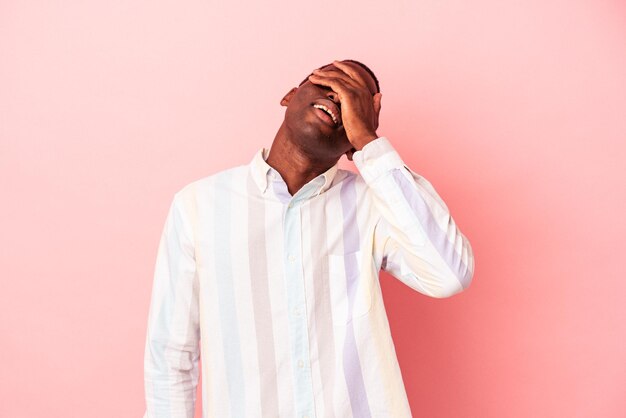 Молодой афроамериканец, изолированный на розовом фоне, радостно смеется, держа руки на голове. Концепция счастья.