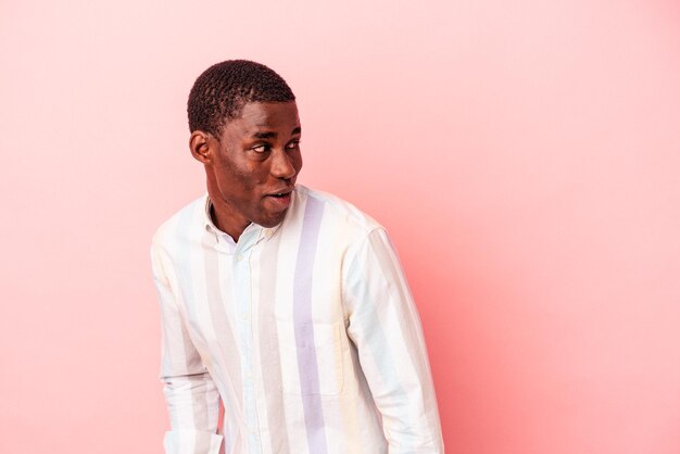 Young African American man isolated on pink background looks aside smiling, cheerful and pleasant.